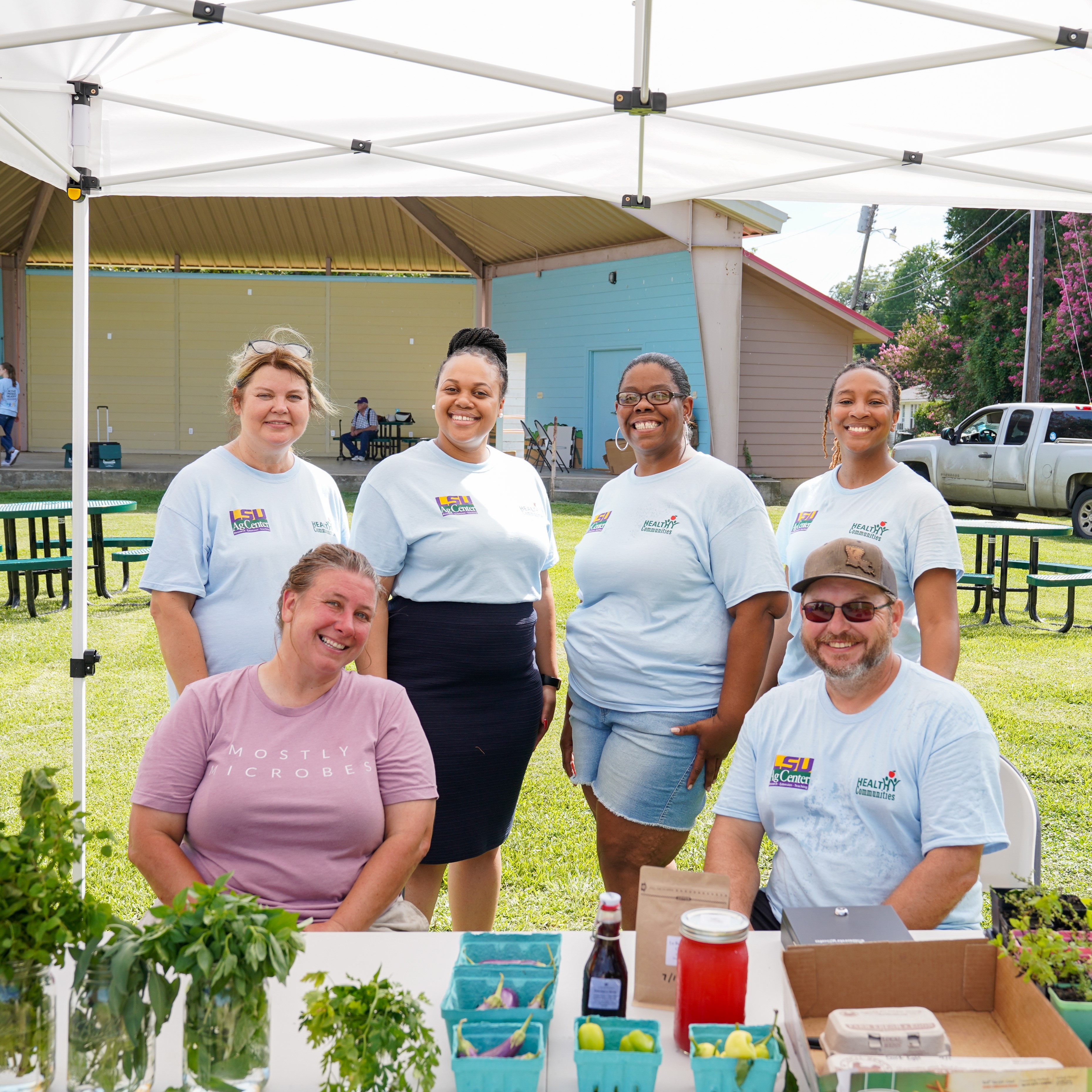 Group of six people smiling and standing behind a table at a farmers' market